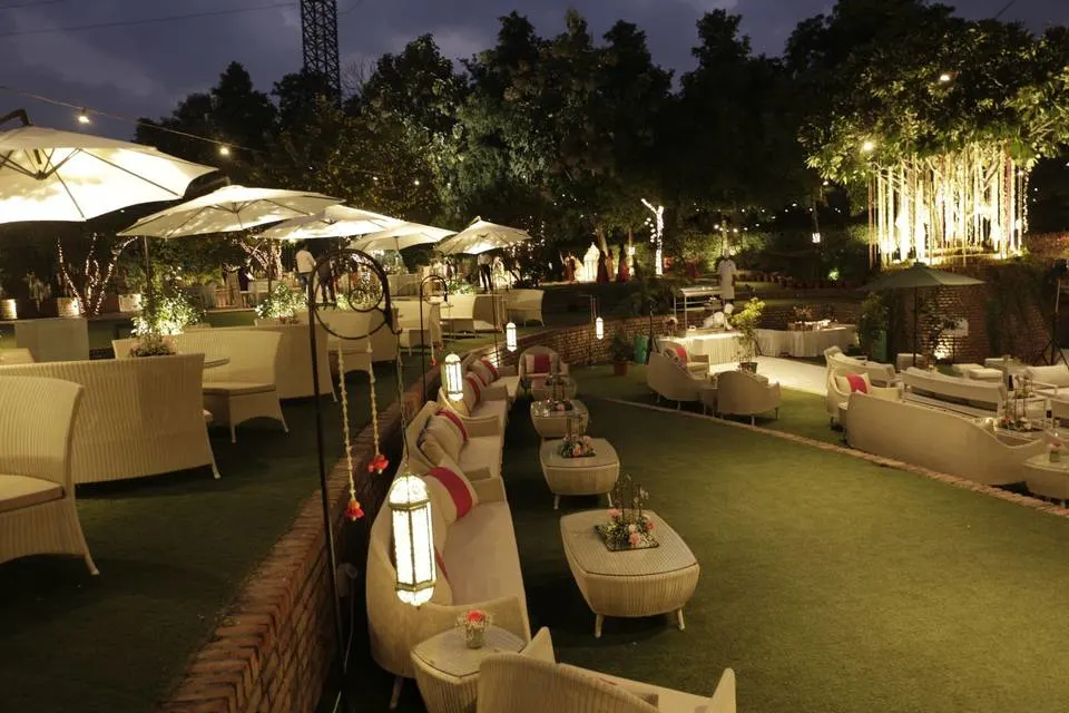 A cozy outdoor wedding venue with ambient lighting, elegant lounge seating, white umbrellas, and lush greenery—ideal for an intimate evening celebration